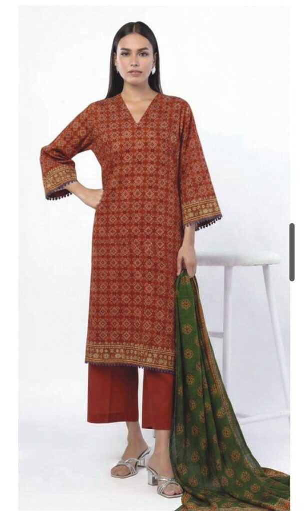 A model wearing a SS2351A 3-piece lawn suit by Khaadi. The outfit features a long kurta with intricate vertical patterns and detailed borders, paired with dyed trousers and a matching printed dupatta with striped and floral designs. The model stands against a plain background, holding the dupatta, with product fabric details displayed on the left side.
