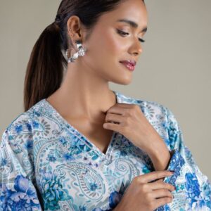 A model wearing a 1-26-143-A-E 2-piece lawn suit by Khaadi. The outfit features a long kurta with intricate vertical patterns and detailed borders, paired with dyed trousers and a matching printed dupatta with striped and floral designs. The model stands against a plain background, holding the dupatta, with product fabric details displayed on the left side.