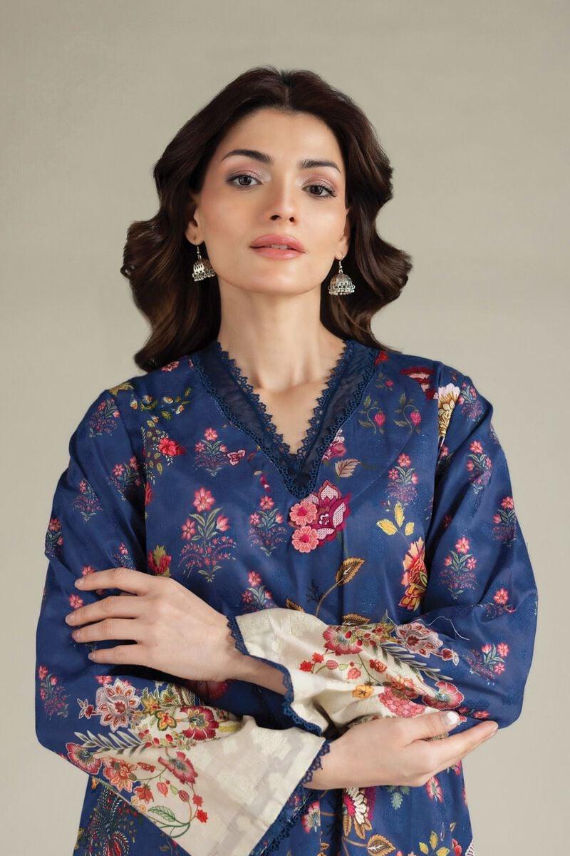 A model wearing a A112-26-101EH1 2-piece lawn suit by Khaadi. The outfit features a long kurta with intricate vertical patterns and detailed borders, paired with dyed trousers and a matching printed dupatta with striped and floral designs. The model stands against a plain background, holding the dupatta, with product fabric details displayed on the left side.