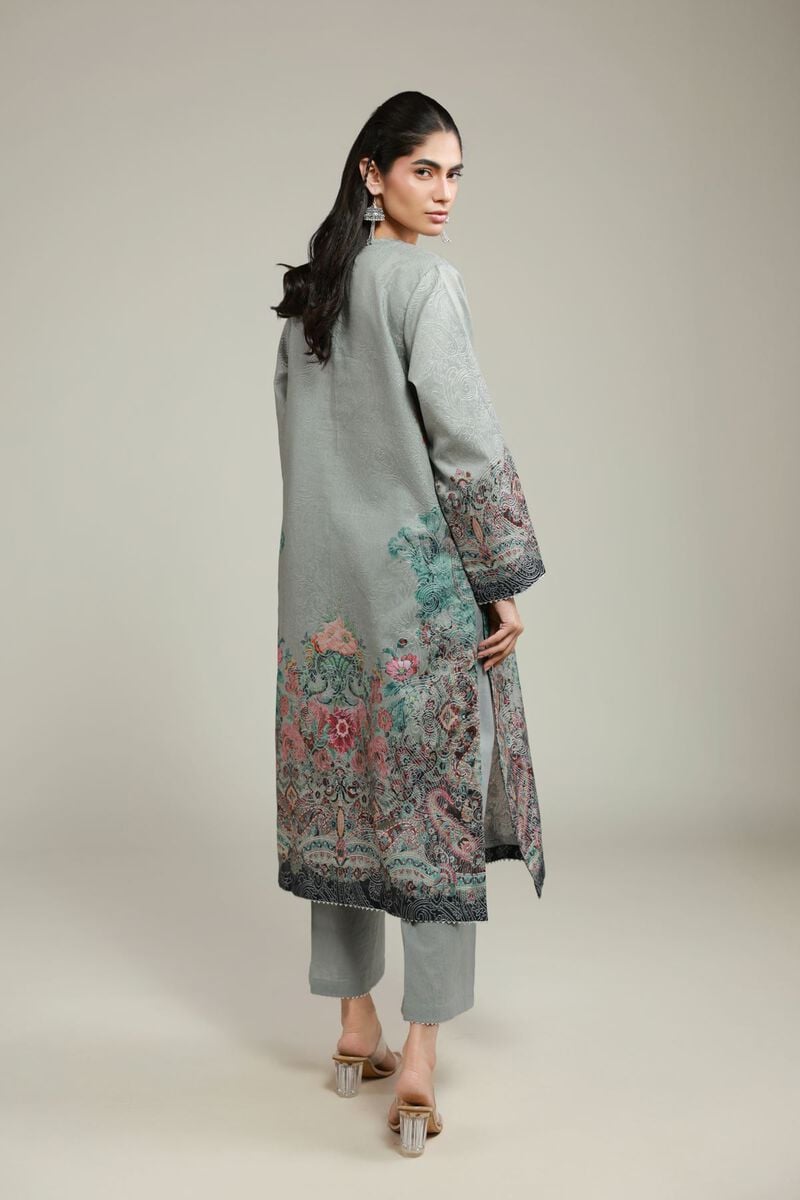 A woman wearing a grey printed kurta with floral patterns near the hem and sleeves, paired with matching straight trousers and transparent heels.