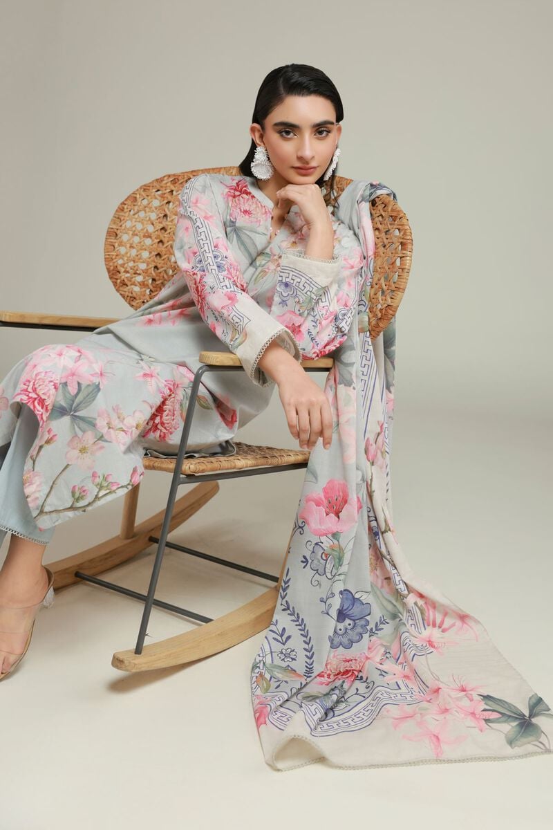 A model wearing a A22-26-103FF1 3-piece lawn suit by Khaadi. The outfit features a long kurta with intricate vertical patterns and detailed borders, paired with dyed trousers and a matching printed dupatta with striped and floral designs. The model stands against a plain background, holding the dupatta, with product fabric details displayed on the left side.