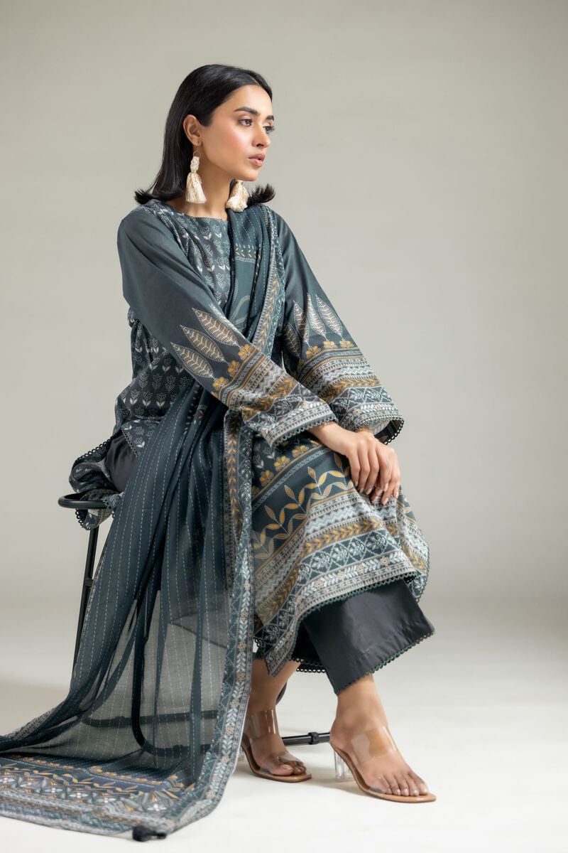 A model wearing a A22-26-115FH1 2-piece lawn suit by Khaadi. The outfit features a long kurta with intricate vertical patterns and detailed borders, paired with dyed trousers and a matching printed dupatta with striped and floral designs. The model stands against a plain background, holding the dupatta, with product fabric details displayed on the left side.